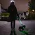 Persoon loopt 's nachts met een kleine hond, hond draagt een lichtgevende groene halsband en de lijn is ook verlicht.