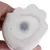 Vue rapprochée du dessous d’un objet en céramique blanche avec un bouchon rond en plastique transparent au centre, tenu par une main.
