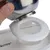 Hand showing how a stainless steel bowl is inserted into the white holder of a feeder. 'Modern Living' logo visible on the holder.