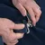 Close-up van handen die een metalen sluiting aan blauwe stof bevestigen. Toont de bediening van het sluitsysteem.