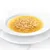 Cuenco blanco con caldo claro y finas tiras de pollo, servido en un plato blanco.