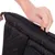 Main ouvrant une fermeture éclair sur un sac ou coussin noir en tissu, poignée visible sur le côté.