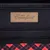 Étiquette en cuir cousue avec le texte « BEST Comfort » sur tissu noir, motif à carreaux rouges et noirs visible en bas de l’image.