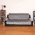 Gesteppter, grauer Sofaschutzbezug aus Stoff auf einem schwarzen Sofa, Bezug bedeckt Sitzfläche, Rückenlehne und Armlehnen.