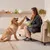 Person sitting on a sofa giving a treat to a dog, demonstrating use of pet food product shown in their hand.