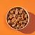 Bowl filled with brown, cube-shaped pet food pieces displayed on an orange background.