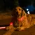 Chien allongé portant une laisse et un collier lumineux rouges visibles dans l’obscurité, sur une route la nuit.