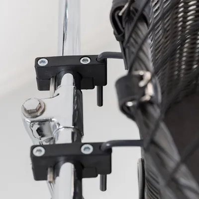 Dettaglio di fissaggio in metallo e plastica di un cestino intrecciato su una barra cromata, con viti e ganci visibili.