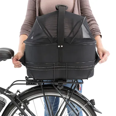 Schwarze Fahrrad-Transportbox mit Netzabdeckung, befestigt am Gepäckträger eines Fahrrads. Person hält die Box an den Seitengriffen.