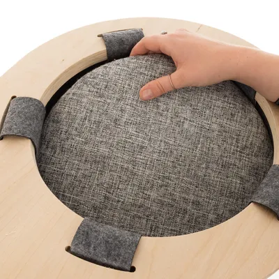 Käsi näyttää irrotettavaa harmaata kangaspäällysteistä tyynyä pyöreässä puukehyksessä, jossa on huopapidikkeet.