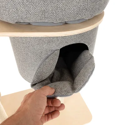 Hand zeigt herausnehmbare, gepolsterte Einlage aus grauem Stoff mit Muster in einer Höhle eines Kratzbaums.