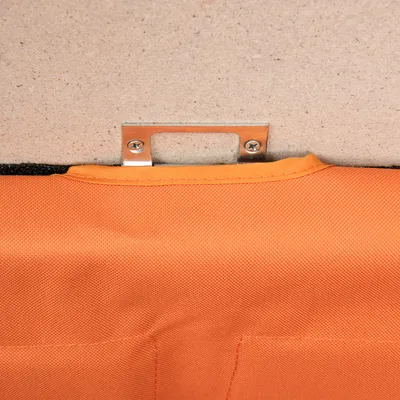 Detailansicht einer orangefarbenen Stofftasche mit Metallhalterung und Schrauben an einer Holzplatte befestigt.