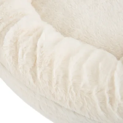 Gros plan sur un panier pour animal en tissu peluche beige, surface douce et rebord rembourré visibles.
