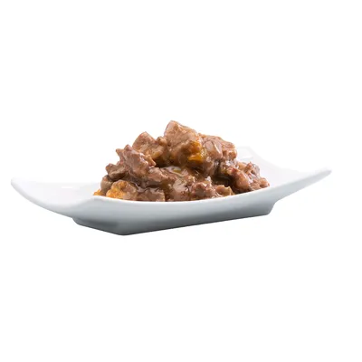 Posnetek od blizu postrežene mokre hrane v beli skledi, sestavljene iz mesnatih kosov v omaki.