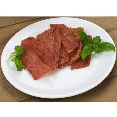 Плоски парчета месо върху бяла чиния, гарнирани със свежи листа босилек. Видими са текстурата на месото и зелените подправки.