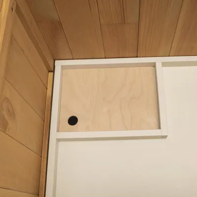 Vista interna di una struttura in legno con parete scorrevole in legno chiaro e foro rotondo, per mostrare la funzionalità o la costruzione del prodotto.