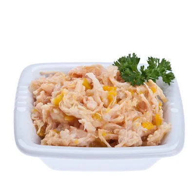 Ciotola bianca con alimento umido a base di carne sfilacciata e pezzetti gialli, guarnito con rametto di prezzemolo. Nessun marchio o testo visibile.