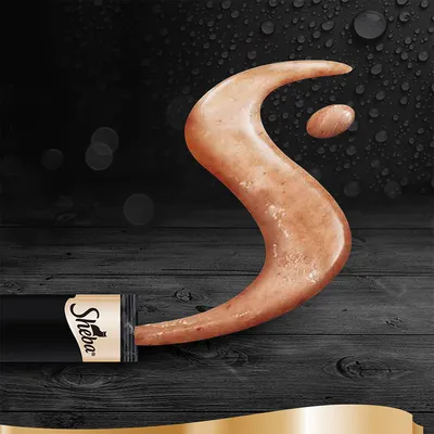 Crema per gatti Sheba spremuta da una confezione nera con logo Sheba visibile, su sfondo scuro con gocce d'acqua.