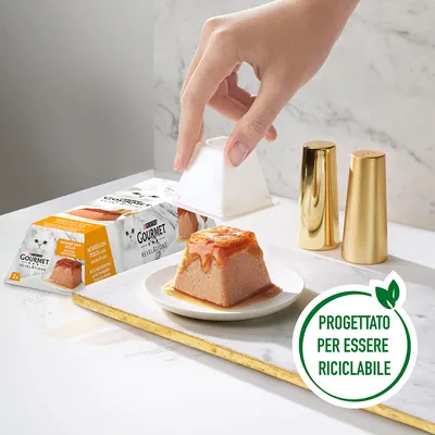 Mousse con pollo Gourmet Revelations per gatti, confezione da 2 vaschette. Mano che serve la mousse su piattino. Testo visibile: Progettato per essere riciclabile.