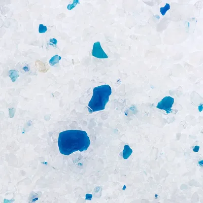 Close-up van kattenbakvulling met witte en blauwe korrels, materiaal lijkt op silicaat. Geen merknaam of tekst zichtbaar.