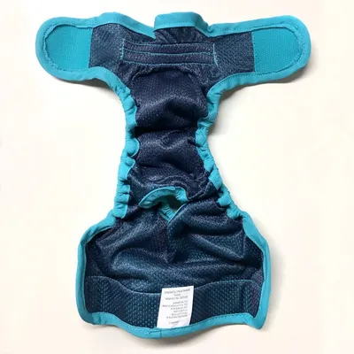 Vista interna di un pannolino per cani blu scuro con bordo turchese e chiusure in velcro. L'etichetta mostra istruzioni di lavaggio e composizione del materiale.