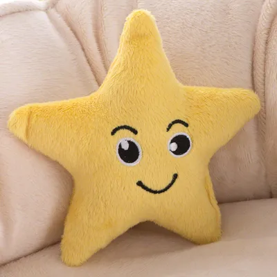 Gelbes Plüschkissen in Sternform mit gesticktem Gesicht, bestehend aus Augen und einem Lächeln. Liegt auf beigem Stoffhintergrund.