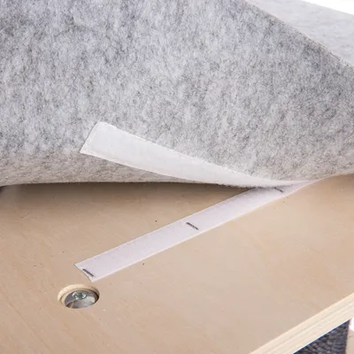 Grauer Filzstoff mit Klettverschluss auf einer Holzplatte, zeigt Befestigungsmethode für Zubehör oder Möbel.