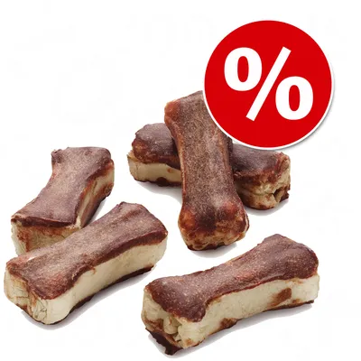 Varios huesos masticables marrones sobre fondo blanco con símbolo de porcentaje en círculo rojo, indicando oferta o descuento visible en la imagen.