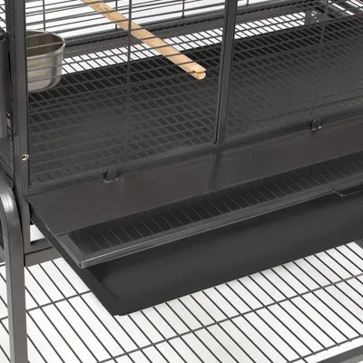Vogelkooi van zwart metaal met houten zitstok, metalen voerbak en uitschuifbare kunststof lade onderin.