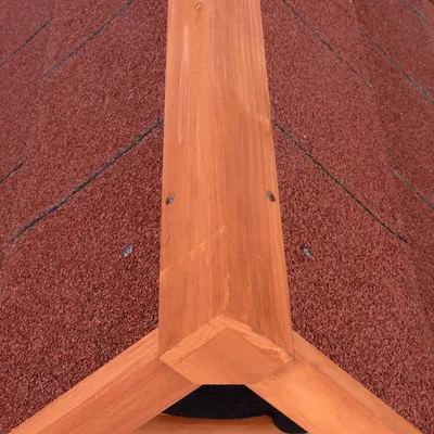 Toit en bois avec bardeaux rouges, vue rapprochée de la faîtière et des vis visibles sur le bois. Matériaux : bois et bardeaux bitumés.