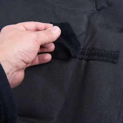 Närbild av en hand som öppnar ett svart kardborreband. Visar funktionen hos bandet på svart tyg.