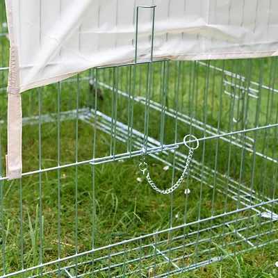 Metalen ren met traliewanden, ketting voor bevestiging en beige afdekking. Ren staat op groen gras.