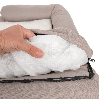 Main ouvrant la housse zippée d’un coussin pour animal, montrant le rembourrage en tissu blanc à l’intérieur du lit beige.