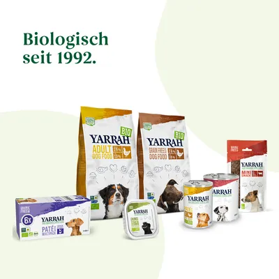Ассортимент кормов для собак Yarrah: сухие и влажные корма, лакомства. Видны упаковки с надписями BIO, Adult Dog Food, Grain Free Dog Food, Mini Snack. Текст на немецком: Biologisch seit 1992.