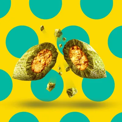 Croquette verte pour animal, sectionnée pour montrer un cœur fourré orange, sur fond jaune à pois turquoise. Aucun texte ou marque visible.