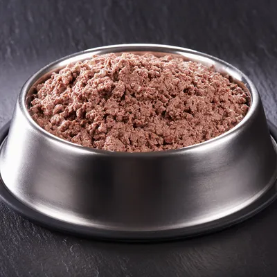 Mokra karma w formie mielonki podana w metalowej misce na ciemnym tle. Widoczna tylko zawartość miski, bez opakowania ani oznaczeń marki.