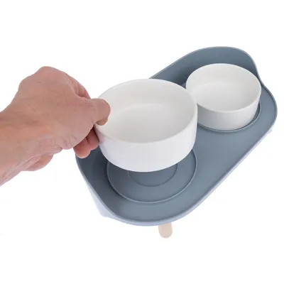 Mão levanta uma taça de comida branca de um conjunto azul de estação elevada com duas taças.
