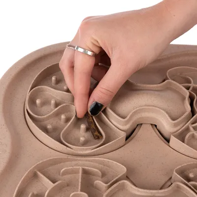Hand places treat in brown intelligence toy with various recesses and obstacles.