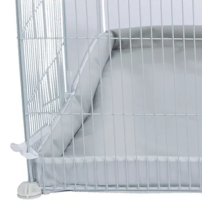 Vue rapprochée d’un coussin gris en tissu placé à l’intérieur d’une cage métallique blanche pour animaux, attaches visibles sur le côté.