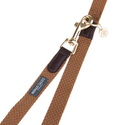 Laisse en tissu marron avec mousqueton métallique doré, détails en cuir foncé et étiquette visible : NOMAD TALES.