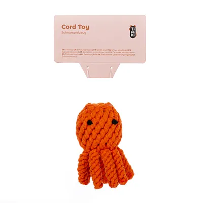 Tiaki Cord Toy, snorlegetøj i orange med sort ansigt. Emballagen viser produktnavn og flersproget beskrivelse.