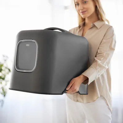 Closed, portable cat litter box in dark grey with transparent entrance and carrying handle.