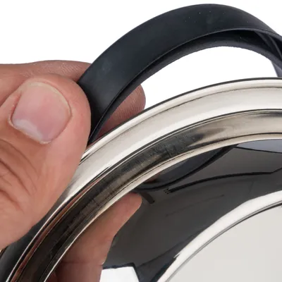 Detailní záběr na víko s černou rukojetí, držené rukou. Ukazuje kvalitu materiálu a úchop produktu.