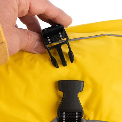 Primo piano di una chiusura a scatto nera su tessuto giallo, aperta da una mano.