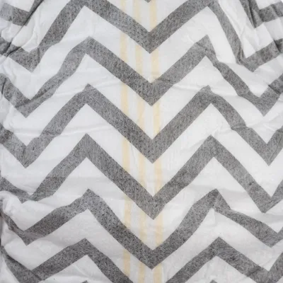 Close-up of white fabric with grey zigzag pattern and yellow stripes. Material texture visible.