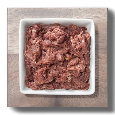 Nahaufnahme von rohem, zerkleinertem Fleisch in einer weißen Schale auf einem Holztisch. Produktdarstellung für Tiernahrung.