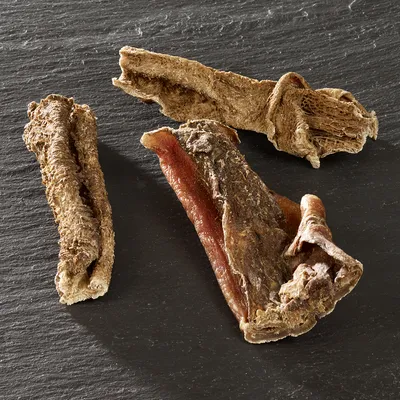 Trois morceaux de friandises séchées pour chien, aspect naturel et rugueux, posés sur une surface noire. Aucun emballage ou marque visible.