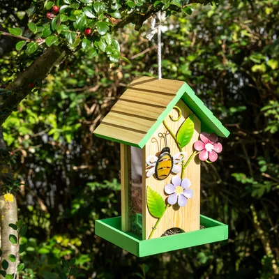 Hängande insekthotell av trä med grönt tak, dekorerat med ett bi och färgglada blommor. Lämplig för trädgården.