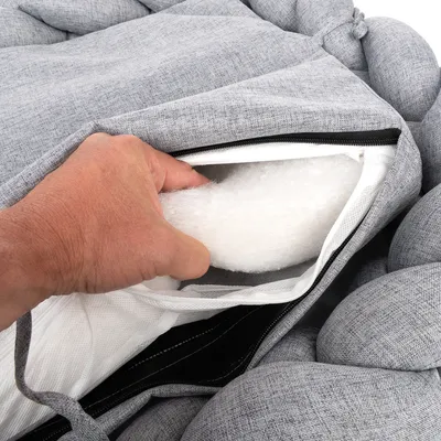 Hand öffnet Reissverschluss eines grauen Kissens, zeigt herausnehmbares Innenpolster aus weissem Material.