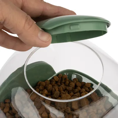 Hand opens green lid of a transparent container with brown dry food pieces.